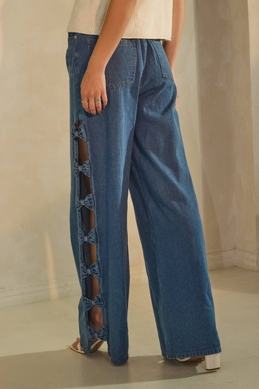 Blue denim pants with unique side cutouts worn by a person on a neutral background