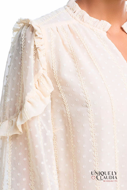 Close-up of a white blouse with ruffled sleeves and lace details, featuring the brand 'Uniquely Claudia'.