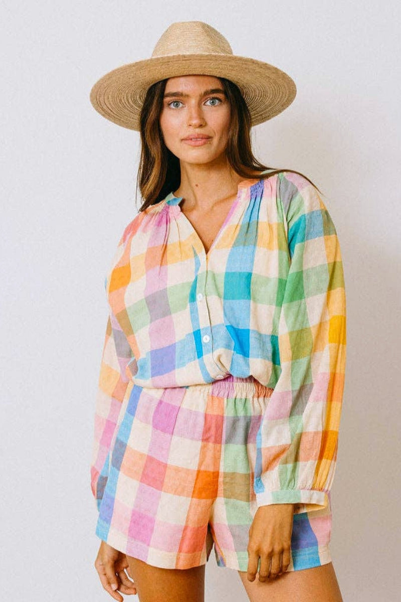 Woman wearing a colorful checkered outfit and straw hat against a plain background