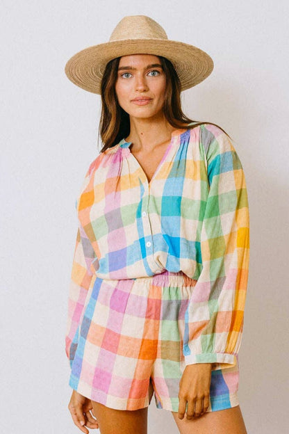 Woman wearing a colorful checkered outfit and straw hat against a plain background
