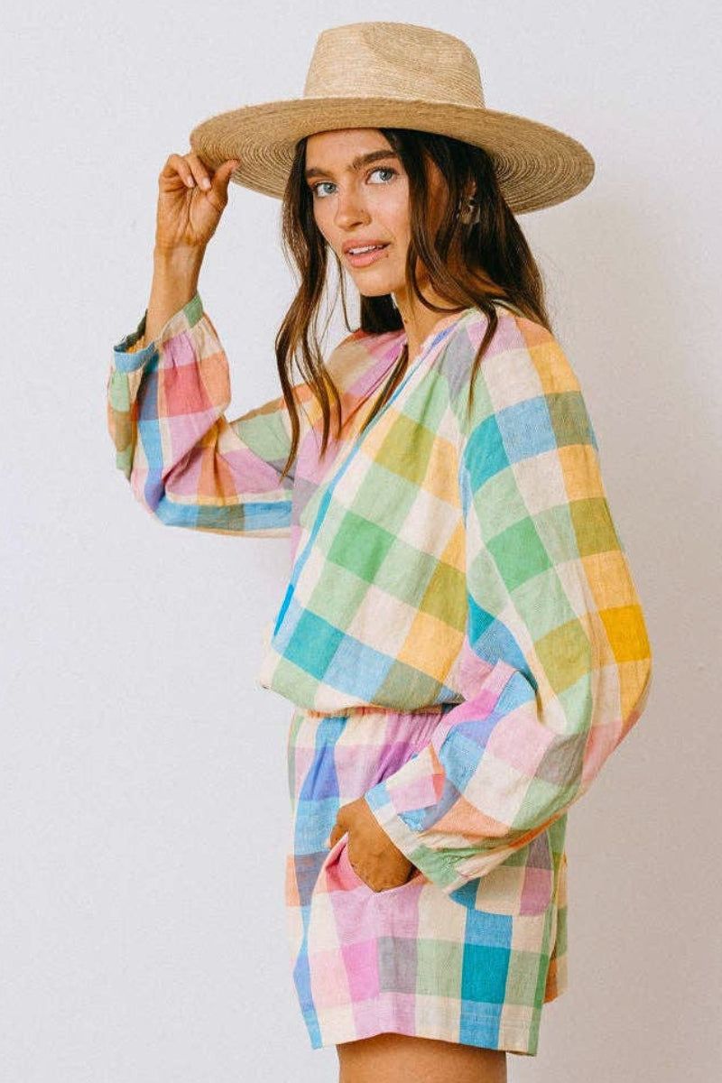 Woman wearing a colorful checkered outfit with a wide-brimmed hat on a plain background