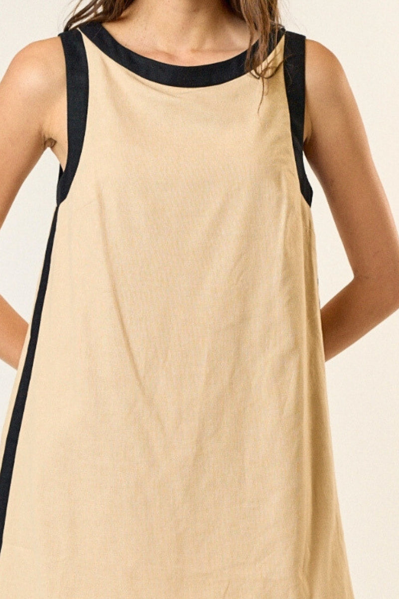 Beige sleeveless dress with black trim worn by a person on a plain background