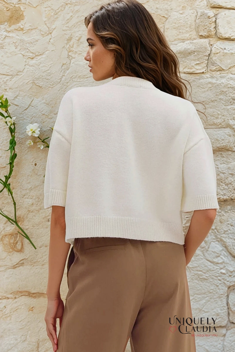 Woman wearing a white sweater and beige pants against a stone wall, with 'Uniquely Claudia' branding.