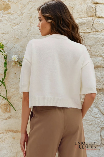 Woman wearing a white sweater and beige pants against a stone wall, with 'Uniquely Claudia' branding.