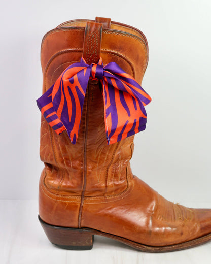 Brown cowboy boot with a colorful bandana tied around it on a white background