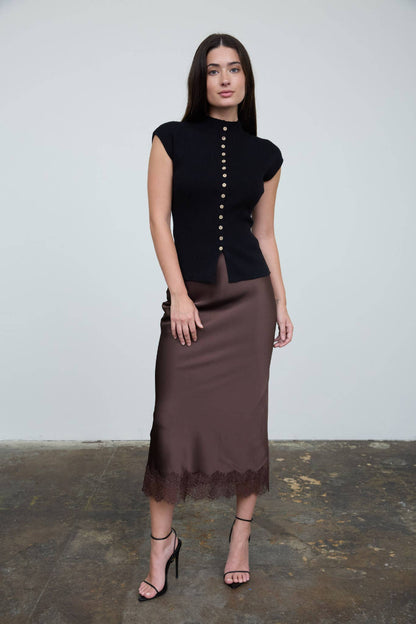 Woman wearing a black top with buttons and a brown skirt on a plain background