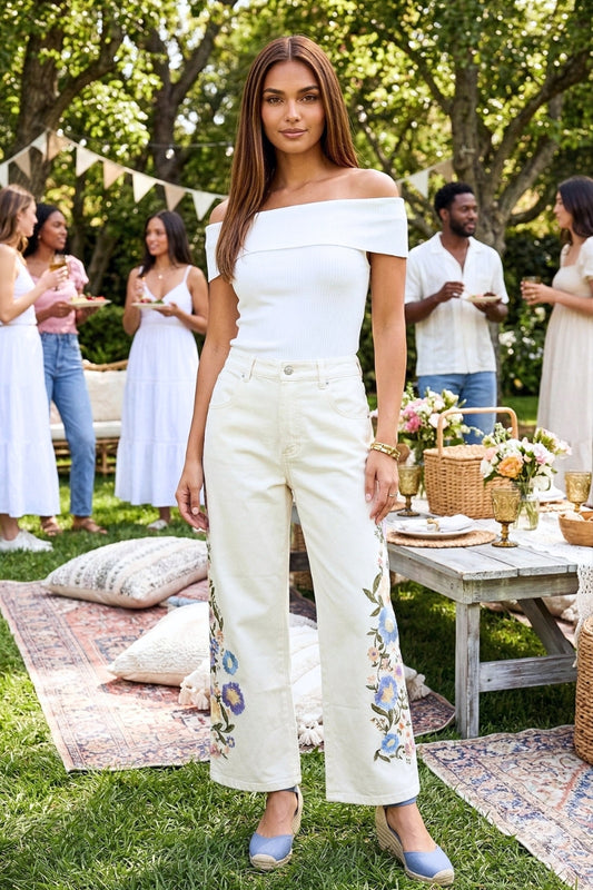 Woman in a white outfit standing outdoors with people and a table in the background