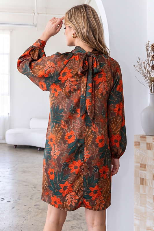 A woman wearing a brown and orange floral print long-sleeve dress, photographed from behind in a bright, modern indoor setting.