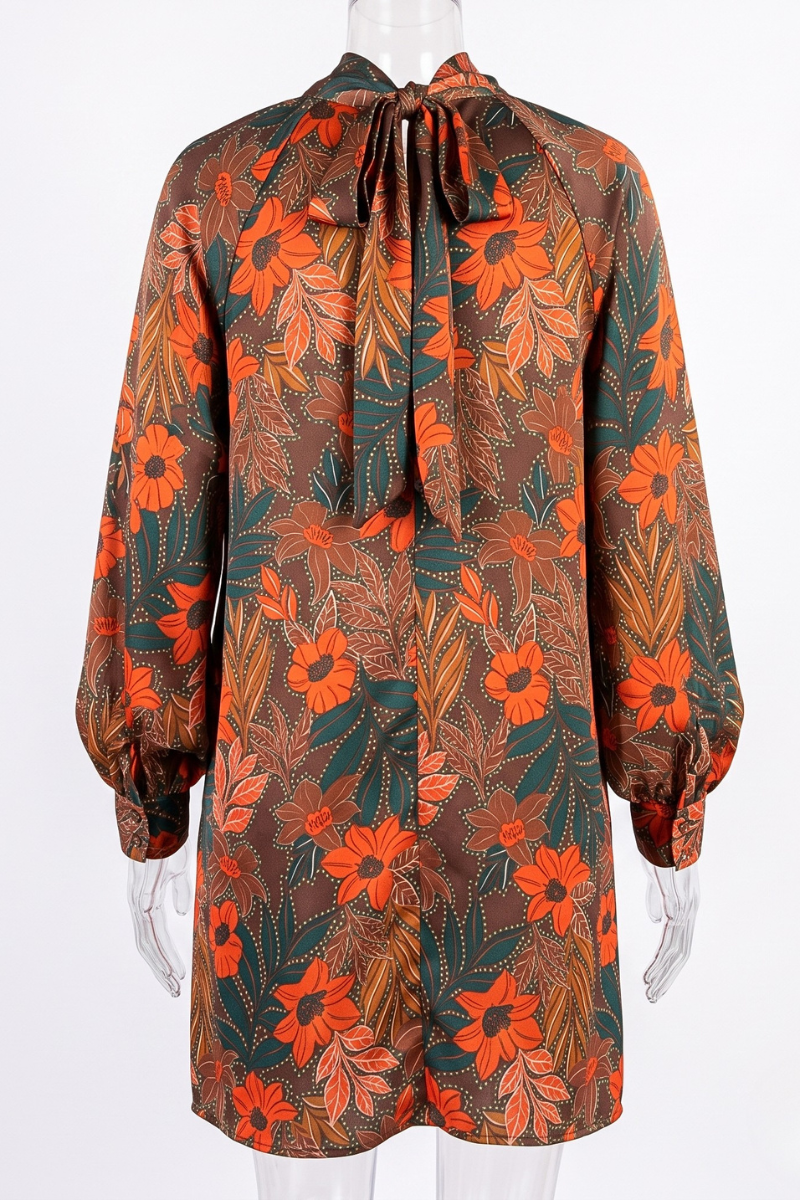 A long-sleeve dress with a high neck and front tie, featuring an all-over floral and leaf print in orange, brown, and dark green, displayed on a mannequin.