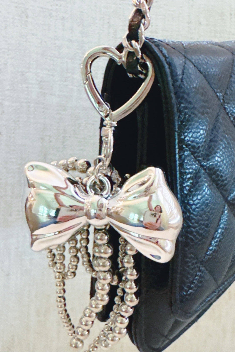 Silver bow keychain with beads hanging from a black quilted handbag.