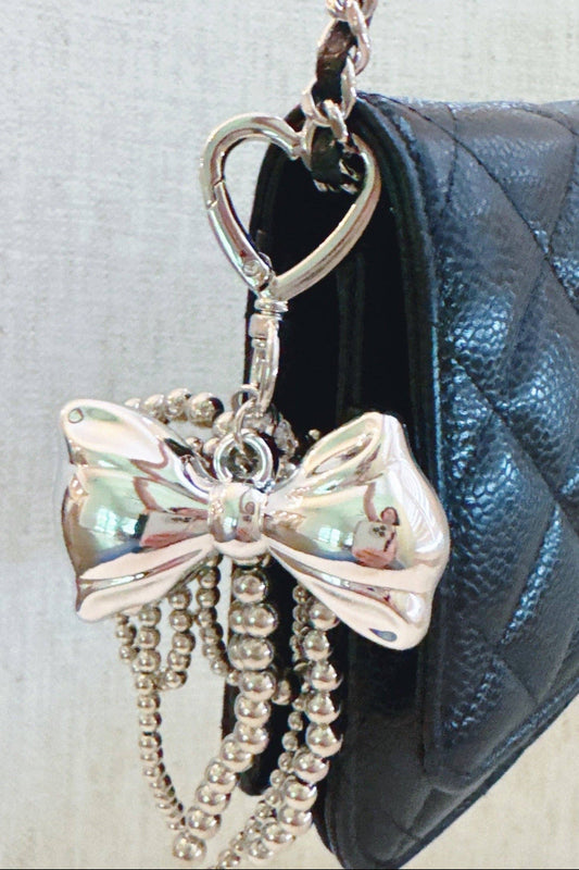 Silver bow keychain with beads hanging from a black quilted handbag.