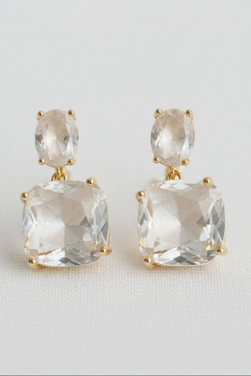 Pair of earrings with clear gemstones and gold accents on a light gray background