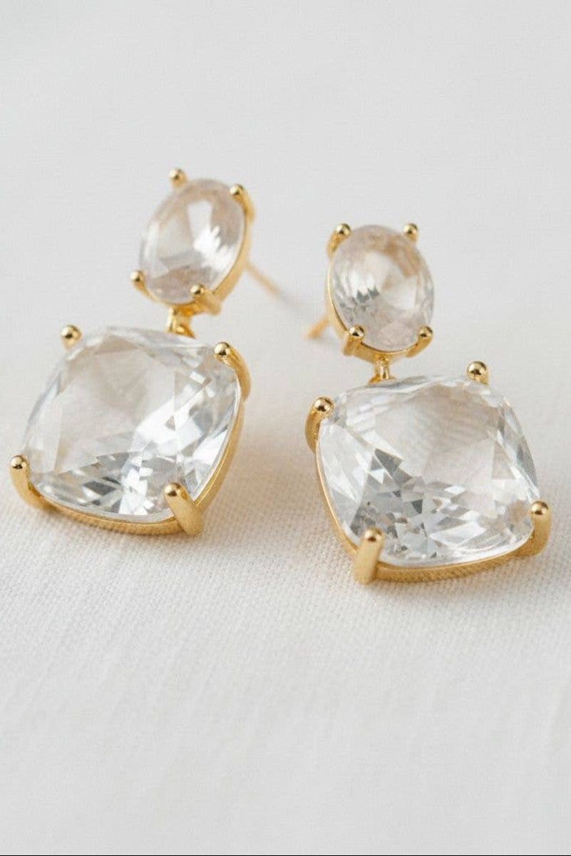 Gold earrings with clear gemstones on a light background