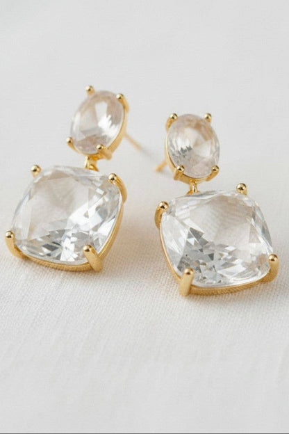 Gold earrings with clear gemstones on a light background