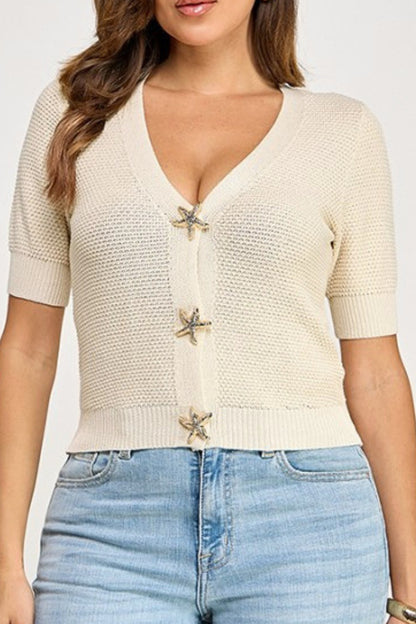 Woman wearing a beige knitted cardigan with starfish buttons and blue jeans on a white background