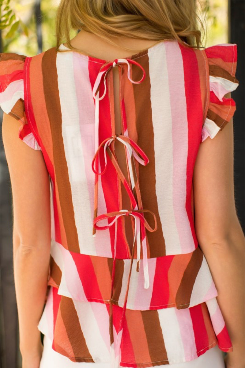 A close-up back view of a woman wearing a sleeveless ruffled top with vertical stripes in red, orange, brown, and white, featuring tie closures at the back.