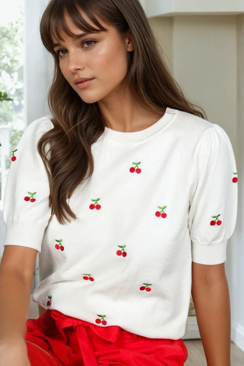 Woman wearing a white t-shirt with red cherry patterns and red pants indoors.