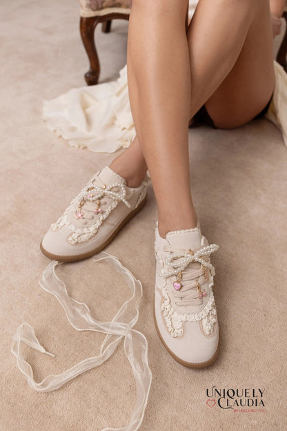 White sneakers with lace details worn by a person on a beige carpet, with 'Uniquely Claudia' branding.