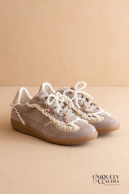 Pair of gray sneakers with white laces on a beige background, featuring the brand 'UNIQUELY CLAUDIA'.