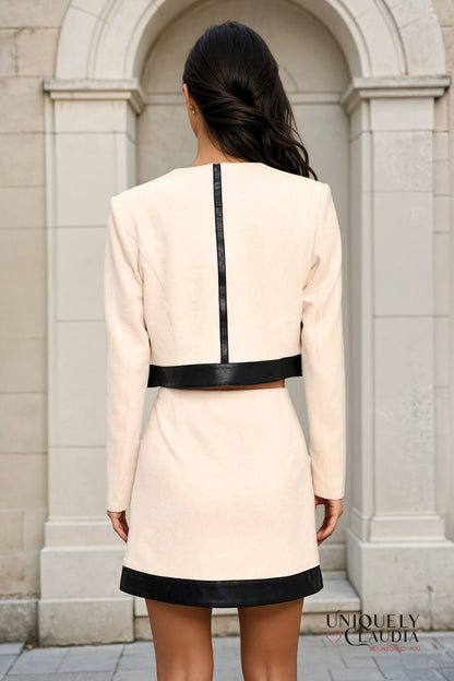 Woman wearing a beige dress with black accents standing against a stone archway.