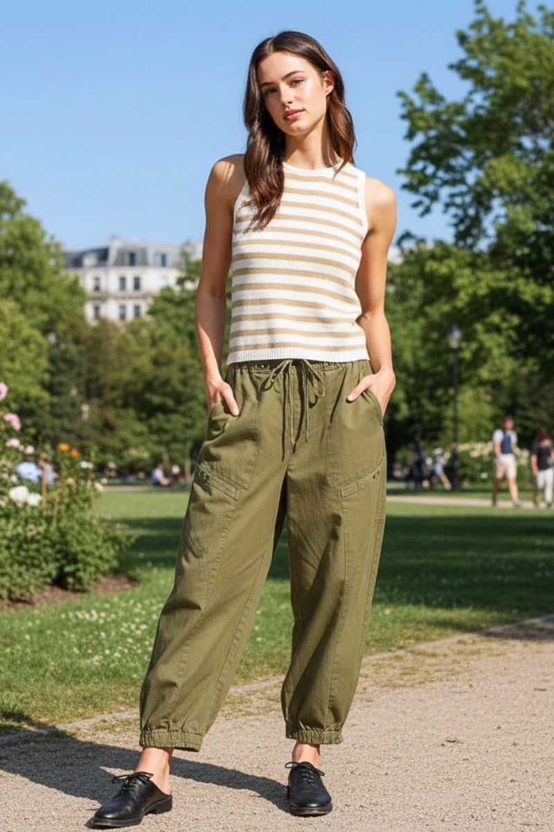 Woman wearing a striped tank top and green pants standing in a park.