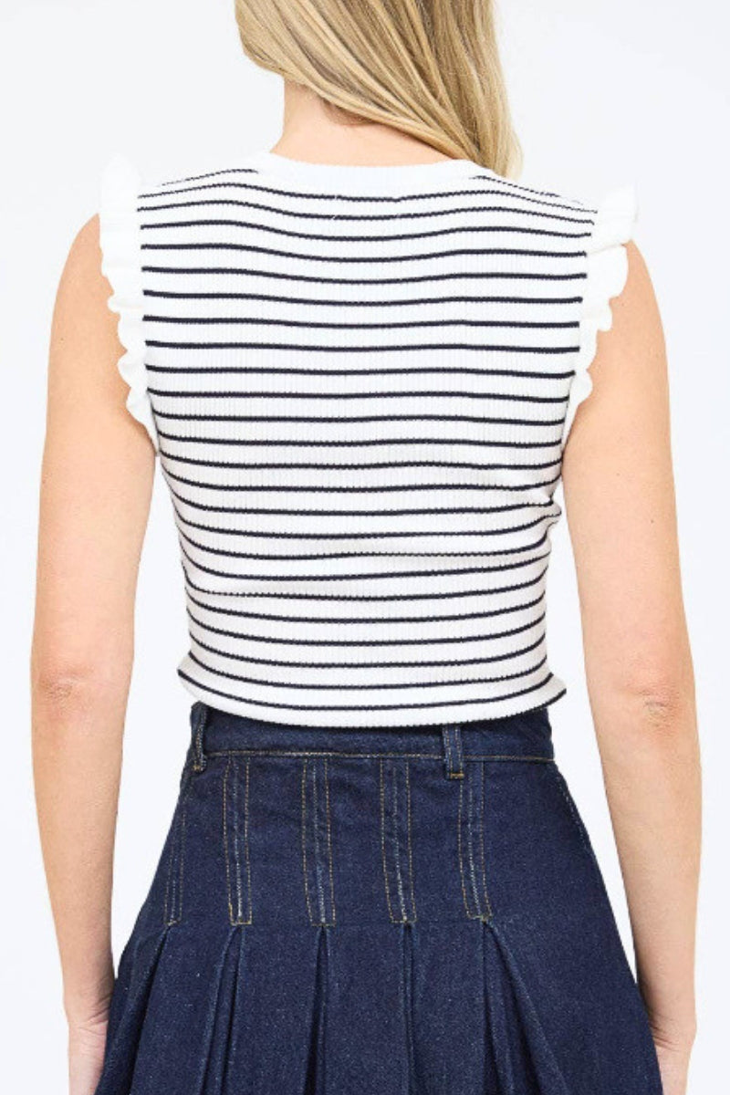 Person wearing a black and white striped sleeveless top with ruffled edges and a navy pleated skirt on a white background.