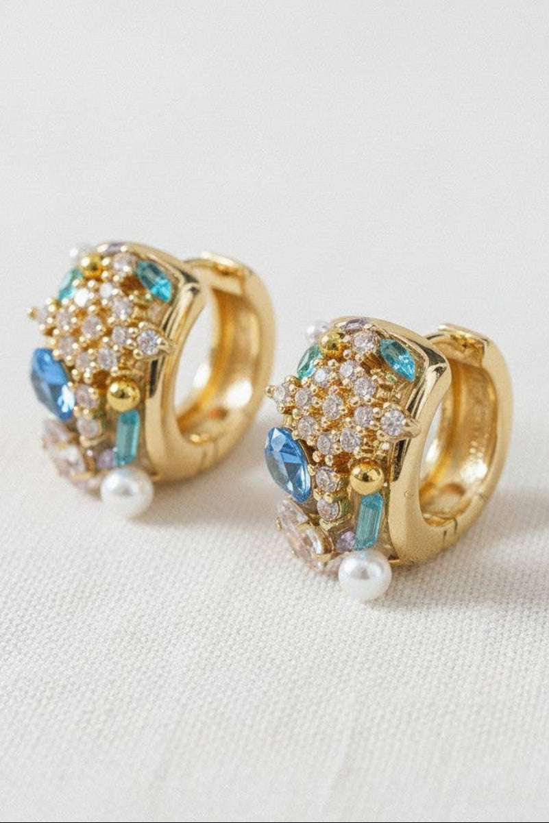 Gold hoop earrings with gemstones and pearls on a light background