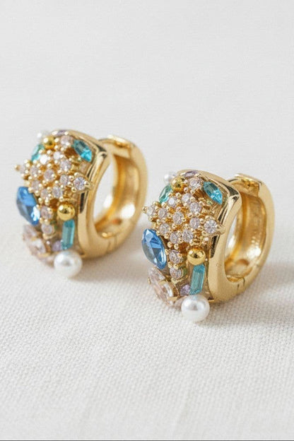 Gold hoop earrings with gemstones and pearls on a light background