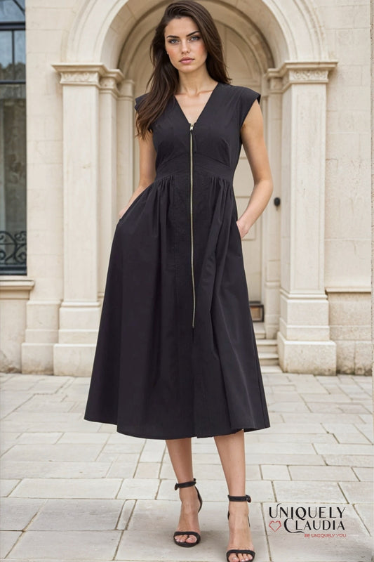Woman wearing a black dress standing in front of a stone archway.