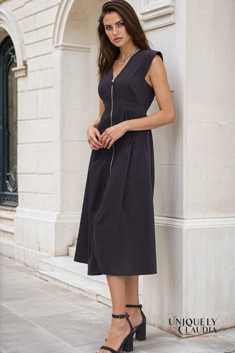 Woman wearing a black sleeveless dress standing against a white stone wall.