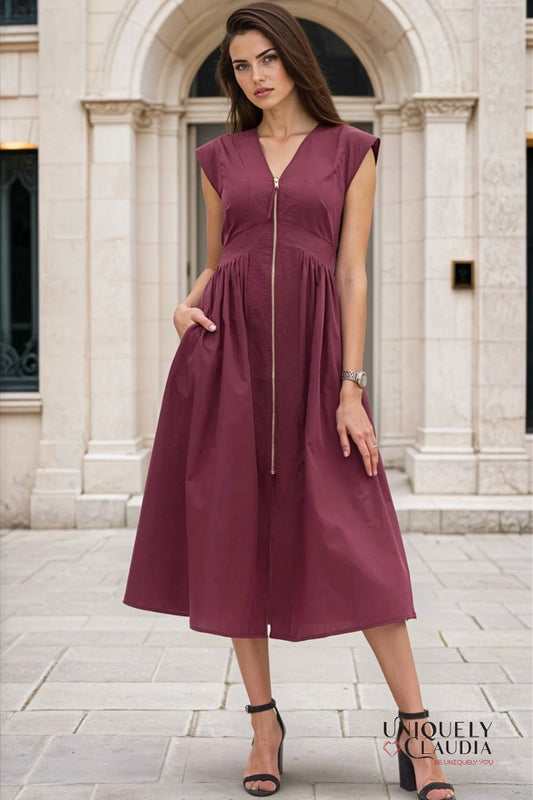 Woman wearing a burgundy dress with a zipper in front, standing in front of classical architecture.