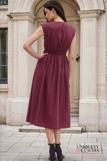 Woman wearing a burgundy dress standing in front of a stone building.