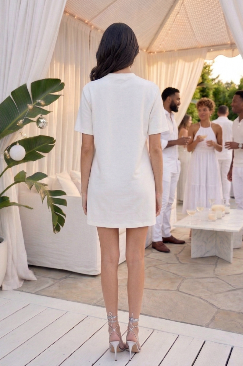 Woman in a white dress standing in front of a white canopy with people in the background.
