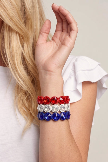 Person wearing a bracelet with red, white, and blue beads on a plain background
