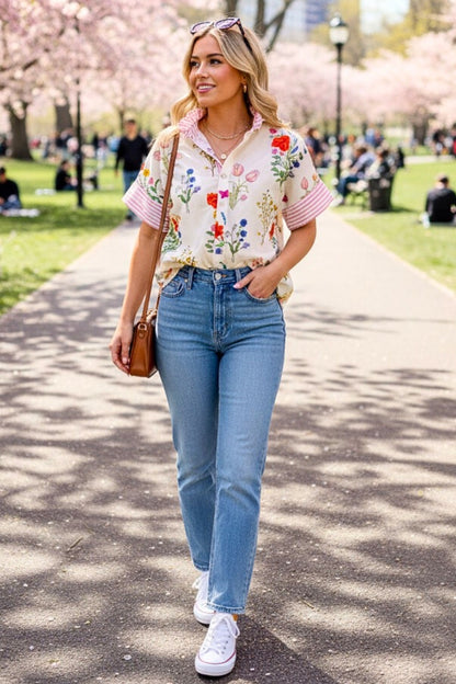 Woman in a floral blouse and jeans walking in a park with cherry blossoms.